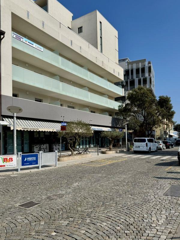 Moderní vícepatrová budova s balkonem a proskleným zábradlím na klidné ulici s modrou oblohou.