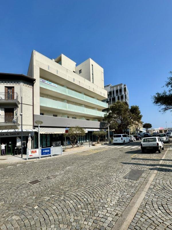 Moderní budova s balkony na rohu dlážděné ulice za slunečného dne.