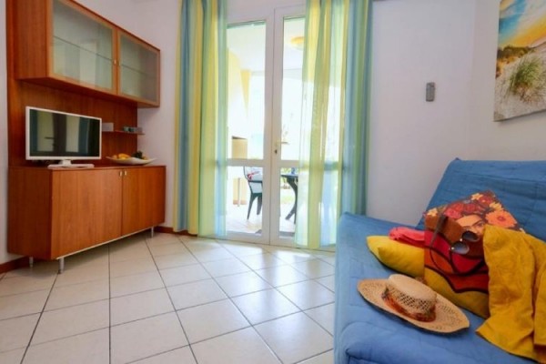 Světlý obývací pokoj s modrou pohovkou, dřevěným nábytkem a balkónovými dveřmi se záclonami.