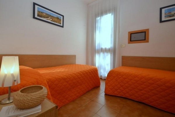 Dva jednolůžkové pokoje s oranžovými přikrývkami a lampou na nočním stolku.