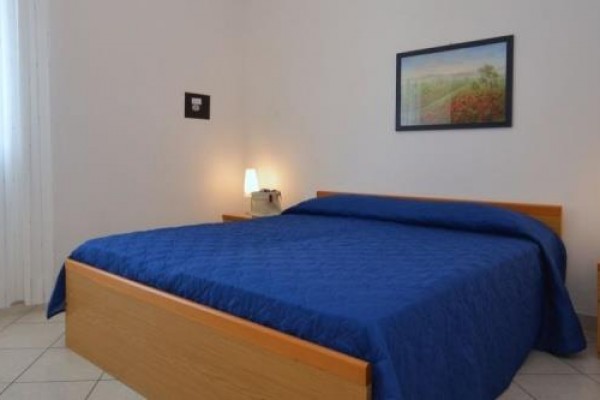 Ložnice s modrým povlečením na posteli a dvěma nočními stolky s lampičkami.