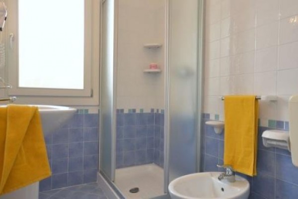 Koupelna s modrými dlaždicemi, sprchovým koutem, umyvadlem a žlutými ručníky.