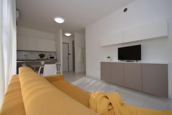 Moderní obývací pokoj s oranžovou pohovkou, kuchyňským koutem a televizí.
