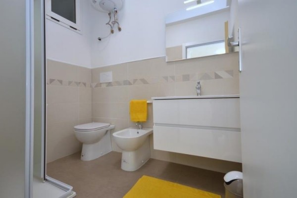 Moderní koupelna s bidetem, toaletou a umyvadlem, doplněná žlutými doplňky.