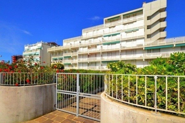 Bytový dům s bílými balkony obklopený zelení pod modrou oblohou.