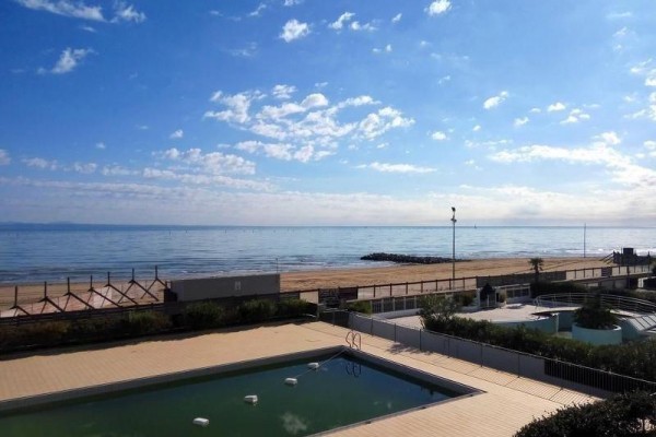 Pohled na bazén, pláž a klidné moře za slunečného dne.