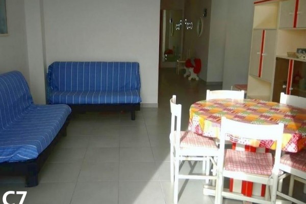 Obývací pokoj s modrými gauči a jídelním stolem s kostkovaným ubrusem.