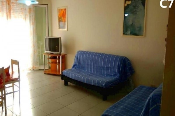 Obývací pokoj s modrým gaučem, starší televizí a obrazy na stěnách.