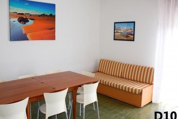 Jídelna s dřevěným stolem, bílými židlemi, oranžovou pohovkou a dvěma obrazy na zdi.