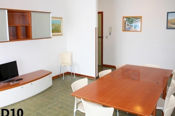 Obytný prostor s velkým dřevěným stolem, židlemi a televizí v rohu.