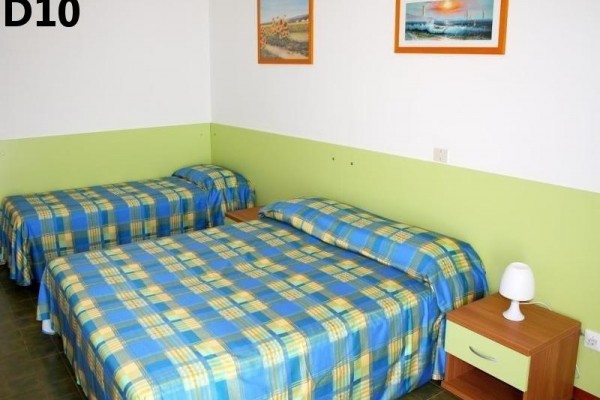 Dva jednolůžkové postele s modro-žlutými kostkovanými přehozy a nočním stolkem s lampou v místnosti.