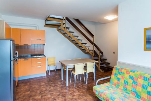 Moderní interiér s kuchyňským koutem, jídelním stolem a schodištěm.