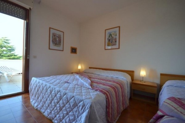Ložnice se třemi postelemi s pruhovaným povlečením a dvěma lampami na nočních stolcích.