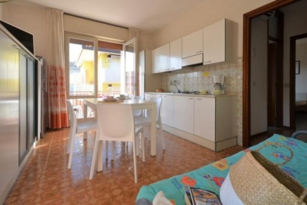 Světlá kuchyň s jídelním stolem a plastovými židlemi vedle otevřených dveří na balkon.