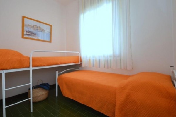 Pokoj se dvěma lůžky a oranžovými přehozy, s obrázkem na zdi a košem pod postelí.